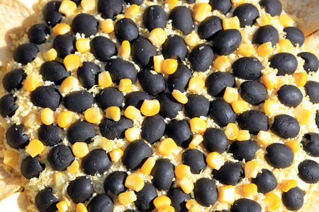 closeup of a salad is decorated in the style of a sunflower, olives, corn and potato chips on a light background in natural lightの写真素材