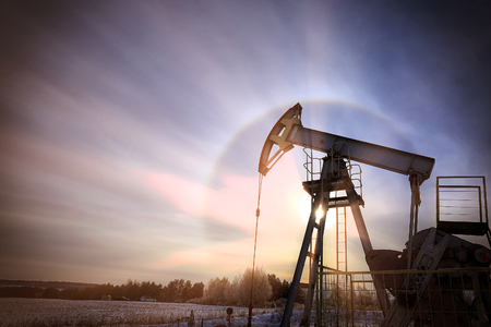 closeup of an oil pump in a snowy field near a forest in the sunlight haloの写真素材