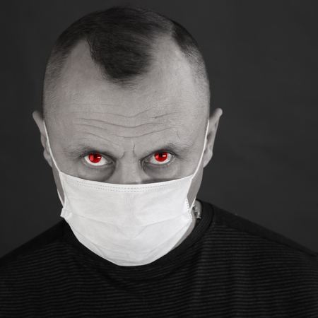 closeup portrait man in a black T-shirt and a medical mask on a gray background studio