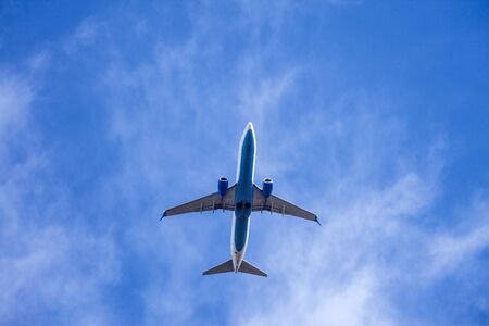 Close-up bottom view of an airplane flying on a sky background with clouds
