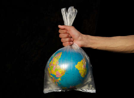 A hand holds a plastic bag with a globe on a black background