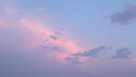 A tranquil sky at dusk with soft pink clouds glowing against a pale blue backdrop. The pastel colors and gentle cloud formations create a serene, dreamy atmosphere suitable for nature, travel, and lifestyle branding, as well as calming backgrounds for messaging and advertising.の素材