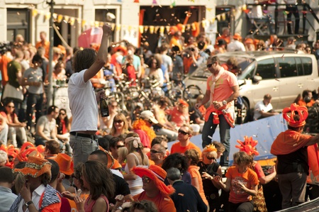 Male party-goer celebrating Dutch national holiday Queen's Day standing on a boat amidst busy Amsterdam canals crowds dressed in orange and confettiのeditorial素材