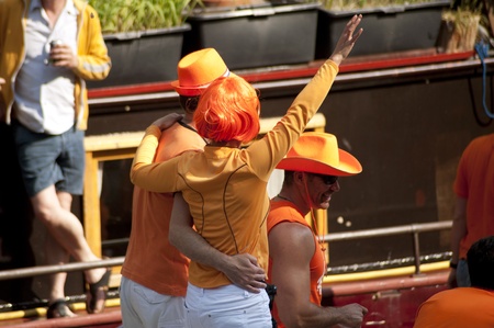 Detail crowd shot of couple dressed in orange fancy dress celebrating Dutch holiday Queen's Day on a boat in Amsterdam canalsのeditorial素材