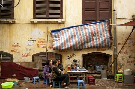 Ha Noi, Vietnam - April, 04, 2009 - Unidentified Women Sitting at Local Food Stall In Front of Old Run Down Buildingのeditorial素材
