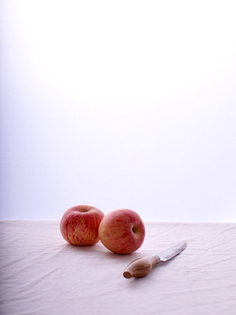 2 red apples next to a sharp knife on a table covered with a white cloth.negative spacesの写真素材
