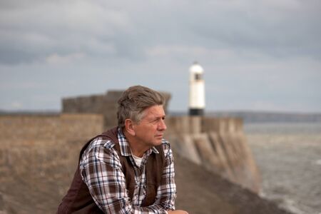 Mature Male looking out to sea with lighthouse in backgroundの写真素材