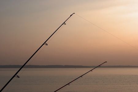 Two fishing rods  with sunset and sea backgroundの写真素材
