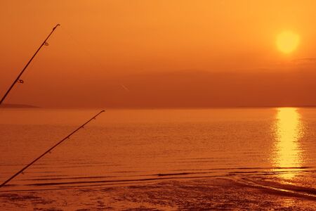 Two fishing rods on a beach at sunsetの写真素材