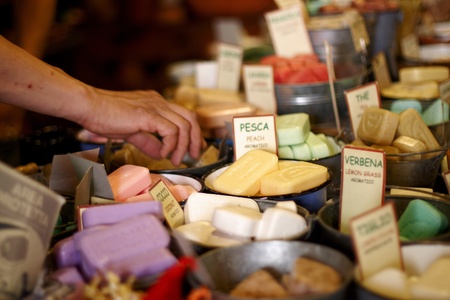 A selection of home made soaps displayed for sale with the hand of a shopper about to pick up the...