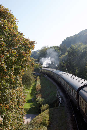 A steam train traveling on the tracks with steam rising in the air