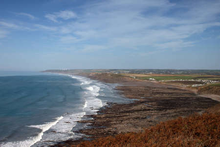 A rugged beach in Cornwall with fifelds and villages in the backgroundの写真素材
