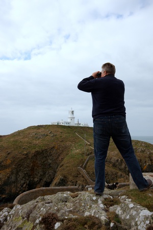 Man looking through binoculars towards Strumble Head lighthouse