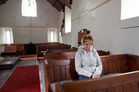 Mature woman sitting in an empty church prayingの写真素材