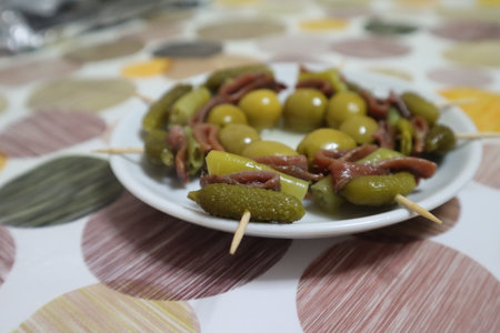 Banderillas, a spanish tapa with olives, anchovies, piparra and pickels in a plate on a tablecloth with circlesの写真素材