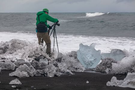 Photographer standing on black sand take pictures the waves. Melting glacier ice In the foreground. Icelandの写真素材