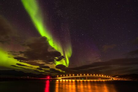 polar lights aurora borealis, northern lights with many clouds and stars in the sky over bridge to Sommaroy , Lofoten islands, Norway, long shutter speed.の写真素材