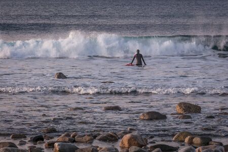 Surfing on picturesque arctic beach on Lofoten islands in Norway, the iconic travel destination for...