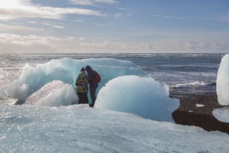 Pieces of melting glacier lying on the black sand. Iceland. Tourists in the background.