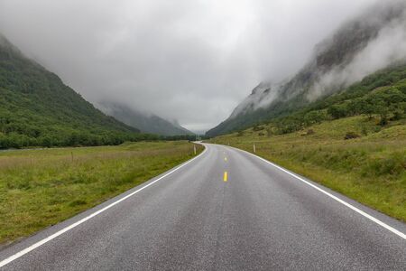 The road leading a mysterious gorge surrounded by clouds of the Norwegian mountains, selective focus
