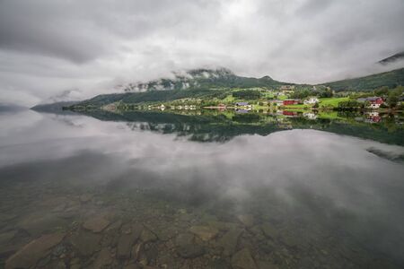 Norwegian fjord and mountains surrounded by clouds, ideal fjord reflection in clear water, selective...