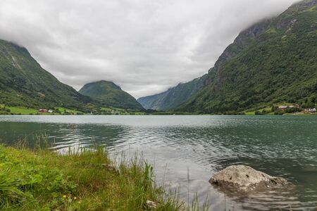 Norwegian fjord and mountains surrounded by clouds, ideal fjord reflection in clear water, selective focusの写真素材