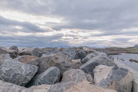Lighthouse in Norwegian fjords, Norway. Sea mountain landscape view. Huge blocks of stones in the foreground. Photo taken at midnight, midnight sunの写真素材