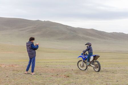 A father photographs a happy son who is sitting on a motorcycle in a helmet in Mongolian Altaiの写真素材