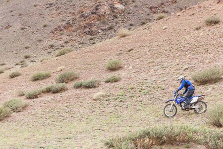 Altai, Mongolia - June 11, 2017: Man riding a motorbike in the steppes of Mongolia, on the hills of Mongolia.の写真素材