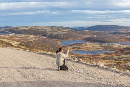 A middle-aged woman sittingin on middle of road and taking photo, travel conceptの写真素材