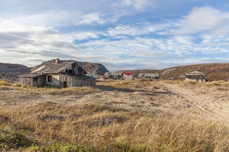Russia, Arctic, Kola Peninsula, Barents Sea, Teriberka: Run down abandoned wooden house in the city center of the old Russian settlement small fishing village with green grass and grey cloudy sky.の写真素材