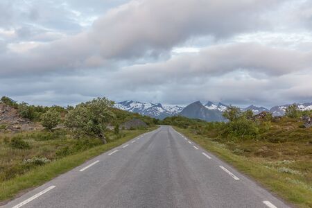 straight and lonely road between norwegian mountains under cloudy sky, selective focusの写真素材