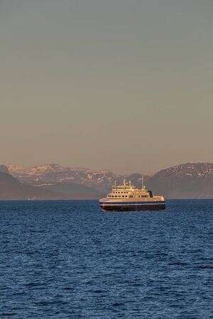 ship sailing on the blue water of the norwegian fjords in polar day, midnight sunの写真素材