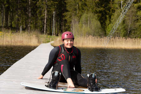 Fagersta, Sweden - Maj 26, 2020: Girl sitting on the pier. Resting after a hard workout. Wakeboarding is heavy extreme sportのeditorial素材