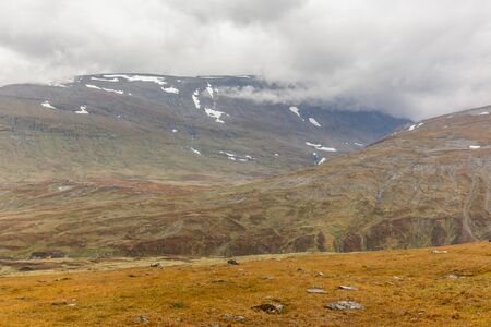 Beautiful wild nature of Sarek national park in Sweden Lapland with snow capped mountain peaks, river and lake, birch and spruce tree forest. Early autumn colors in stormy weather. selective focusの写真素材