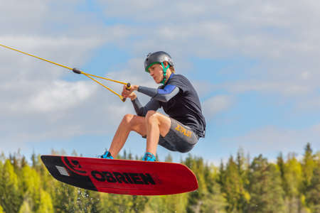 Fagersta, Sweden - Maj 26, 2020: Wakeboarding. Teen Wakeboarder makes extremely difficult jump in air on wakeboard. Guy flies in the skyのeditorial素材