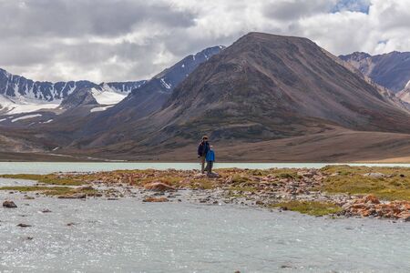 Father and son are walking along the grass near the mountain lake of the Mongolian Altai.の写真素材