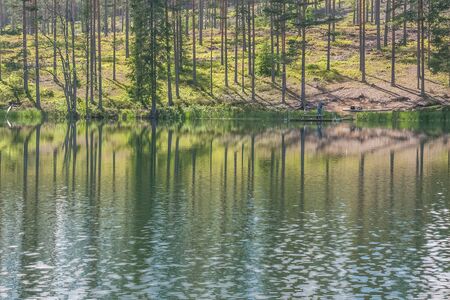 Cloudy sky and tree reflection in secluded area by the lake. Calm waters and cloudy sky. fisherman in the background Sweden. selective focus. long exposureの写真素材