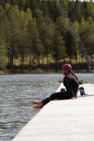 Fagersta, Sweden - Maj 26, 2020: Girl sitting on the pier. Resting after a hard workout. Wakeboarding is heavy extreme sportのeditorial素材