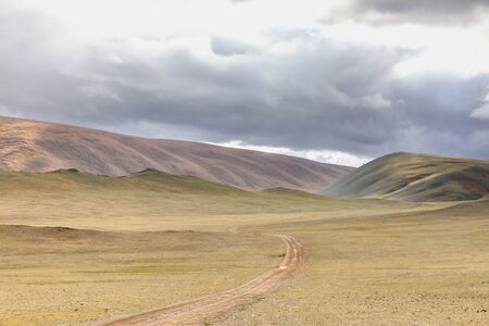 Winding dirt road through lush rolling hills of Central Mongolian steppe. Mongolian Altai. Typical view of Mongolian landscape.の写真素材
