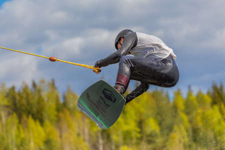 Fagersta, Sweden - Maj 26, 2020: Wakeboarding. Teen Wakeboarder makes extremely difficult jump in air on wakeboard. Guy flies in the skyのeditorial素材