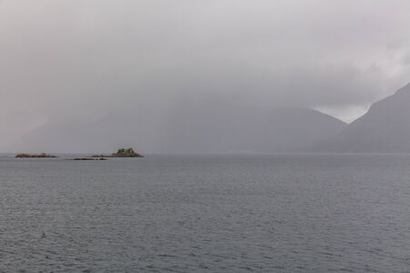 Norwegian fjord and mountains surrounded by clouds, midnight sun, polar day, ideal fjord reflection in clear water. selective focus.の写真素材