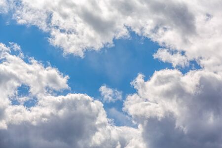 fluffy white clouds against a blue sky backlit by the sun.の写真素材