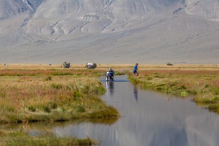 A motorcyclist pushes a motorcycle along a road flooded with water. Altai, Mongoliaの写真素材