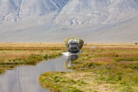 Altai, Mongolia - June 14, 2017: Truck carrying hay on a road covered with water after a flood. Altai, Mongoliaの写真素材