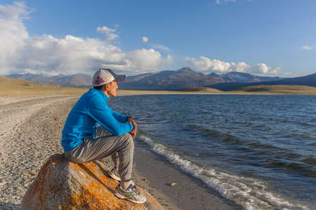 Altai, Mongolia - June 14, 2017: guy on stone on the shore of a mountain lakeのeditorial素材