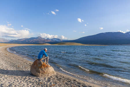 Altai, Mongolia - June 14, 2017: guy on stone on the shore of a mountain lakeのeditorial素材