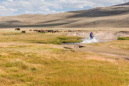 A motorcyclist tries to drive along a road filled with water during a flood after rain. Horses on the back plane.の写真素材