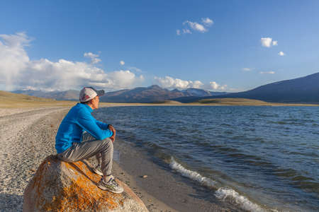 Altai, Mongolia - June 14, 2017: guy on stone on the shore of a mountain lakeのeditorial素材