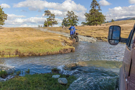 Altai, Mongolia - June 14, 2017: A motorcyclist pushes a motorcycle along a road flooded with water. Altai, Mongoliaのeditorial素材